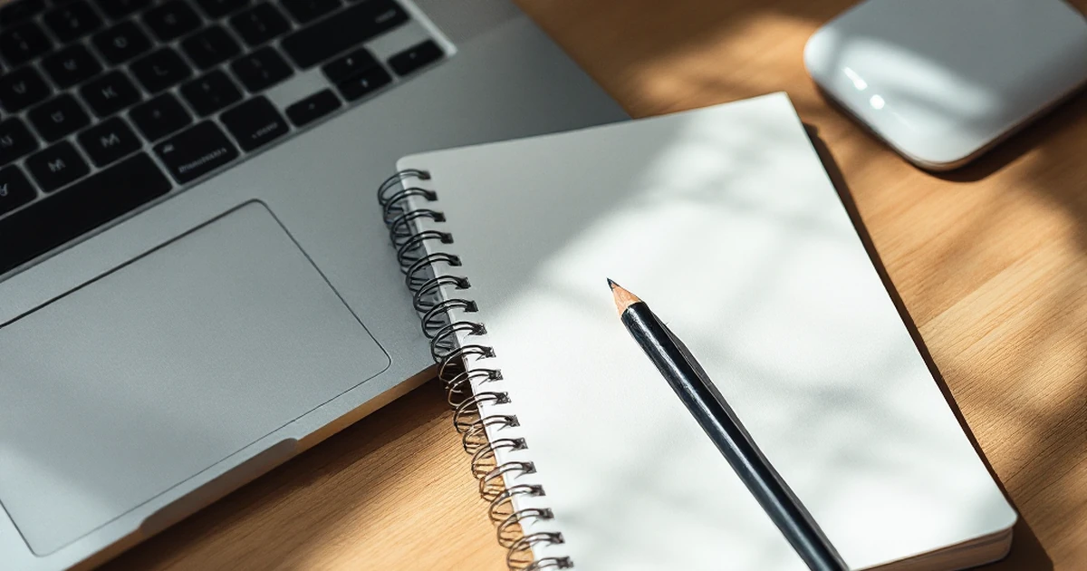 Workspace with closed laptop, notepad, pencil, and Wi-Fi router.